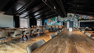 Foto eines Innenraums der Brauerei Maisel aus Bayreuth. Man sieht ein Besprechungszimmer mit großem Holztisch und einer Grafitywand.