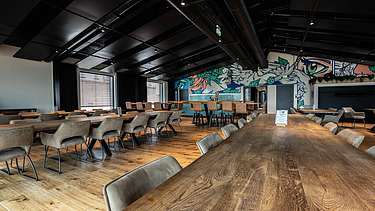 Photo of an interior of the Maisel brewery in Bayreuth. You can see a meeting room with a large wooden table and a graphic wall.