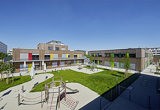 Foto einer Schule aus Holz von außen. Man sieht das Holzgebäude und den Gartenbereich.