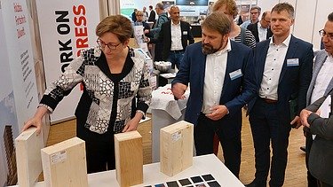 Photo of a trade fair situation with several people examining wood samples.