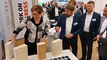 Foto von einer Messesituation mit mehreren Menschen die Holzmuster begutachten.