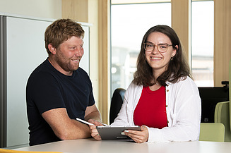 Photo of two people standing at a meeting table.