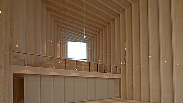 Photo of the interior of the Immanuel Church in Cologne. You can see an empty, high room with wooden walls and a wooden ceiling.