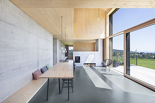 Foto eines modernen Holzhauses mit Holzfassade. Innenaufnahme Esszimmer. Holz- Glas- und Betonwände.