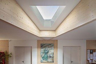 Photo of an interior with wooden ceiling and triangular window. A picture hangs on the wall.