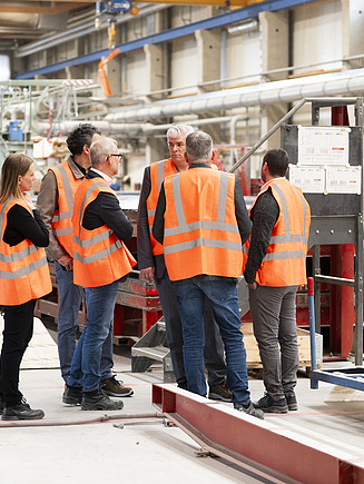 Sechs Personen, die sich in der Fertigungshalle von ZÜBLIN Timber unterhalten.