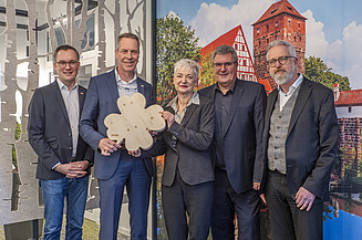 News ZÜBLIN Timber. Order placed by the Martin-Behaim-Gymnasium in Nuremberg Photo with four people. Two of them are holding a wooden shamrock.