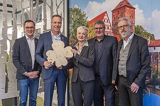 News ZÜBLIN Timber. Order placed by the Martin-Behaim-Gymnasium in Nuremberg Photo with four people. Two of them are holding a wooden shamrock.