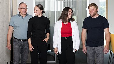 Foto von vier Personen, die im Büroflur entlang gehen.
