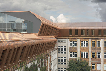Foto einer Luftaufnahme eines mehrgeschossigen Gebäudes. Metropolitan School Berlin. Die Aufstockung aus Holz hat eine brozener Blechverkleidungg.