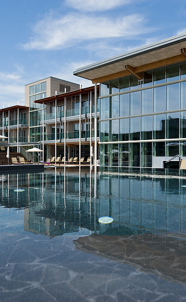 Foto des Hotels Aqualux ini Bardolino. Zu sehen ist ein großes Gebäude mit Glasfassade und Flachdach, zudem ein Pool.