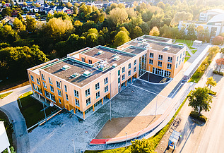 Universität, Witten-Herdecke Foto der Uni Witten von außen. Man sieht ein großes Gebäudes aus Holz.