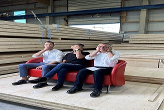Photo of three men sitting on the red couch in the ZÜBLIN Timber factory hall.