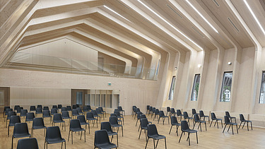 Foto eines bestuhlten Saals mit großer sichtbarer Rippen-Holzkonstruktion.