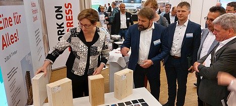 Photo of a trade fair situation with several people examining wood samples.