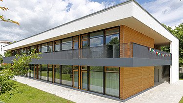Foto einer Außenaufnahme der Kindertagesstätte in Frankfurt. Das Holzgebäude hat ein Flachdach und eine Holz- Glasfassade.