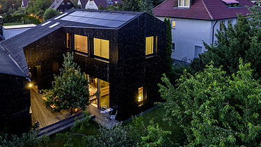 Foto eines Wohnhauses aus Holz und mit dunkler Holzfassade. Abendstimmung.