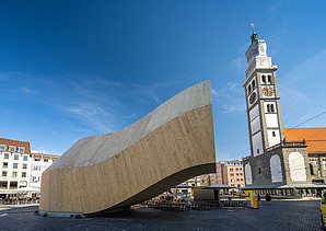 Foto des NEXT500-Pavillons auf dem Augsburger Marktplatz. Sie können ein modernes Holzgebäude sehen.
