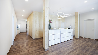 Photo of a reception area in a doctor's surgery. Many wooden surfaces can be seen. LENO-BSP.