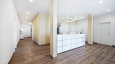 Photo of a reception area in a doctor's surgery. Many wooden surfaces can be seen. LENO-BSP.