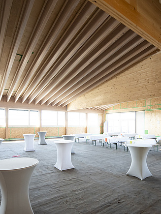 Photo of an interior with wooden ceiling. Topping-out ceremony for the school on the slope.