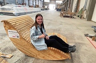 Aktuelles ZÜBLIN Timber Foto einer jungen Frau in der Werkshalle von ZÜBLIN Timber. Sie sitzt auf einer Holzliege.