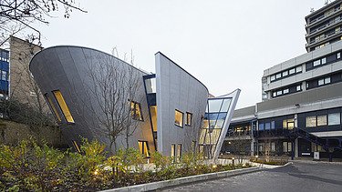 Photo of a building with a wooden façade and sloping walls. You can see another large building in the picture.