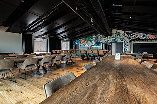 Photo of an interior of the Maisel brewery in Bayreuth. You can see a meeting room with a large wooden table and a graphic wall.