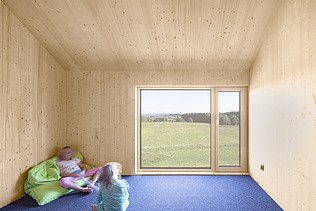Foto eines modernen Holzhauses mit Holzfassade. Innenaufnahme Kinderzimmer. Sichtbare LENO-Holzwände.