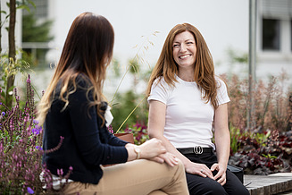 Photo of two young women sitting outside and talking to each other