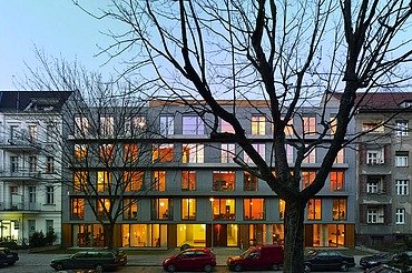 3xGRÜN, Berlin Photo of a multi-storey building in dim light. Leafless trees stand in front of it.