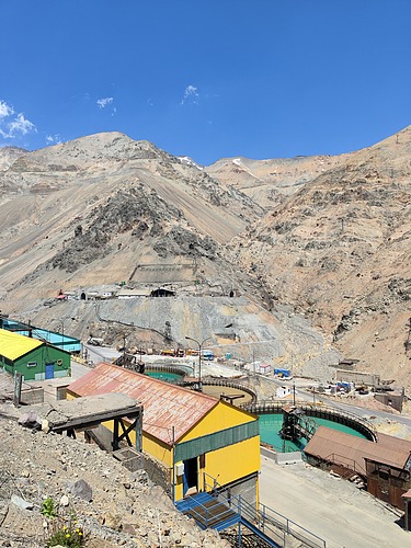 Photo of a barren mountain landscape made of sand. Small houses can be seen in the copper landscape. As well as a blue sky.