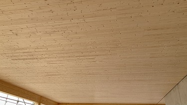 Foto eines Rohbaus aus Holz. Man sieht einen Innenraum mit Holzdecke