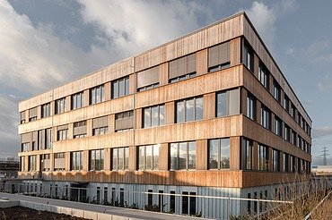Bürogebäude Flexim Berlin Foto de Bürogebäudes Flexim Berlin von außen. Zu sehen ist ein großes Gebäude aus Holz mit Holzfassade und Flachdach.