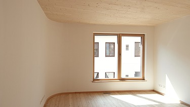 Foto eines Wohnhauses aus Holz. Detailbild unmöbliertes Wohnzimmer mit sichtbarer LENO-Holzdecke.