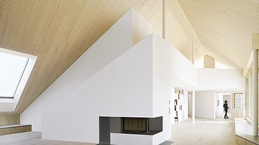 Photo of a modern interior with a striking wood-burning stove in the middle of the room and visible sloping LENO wall elements.