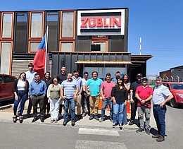 Photo of a group of 17 people. A building with a large ZÜBLIN logo and blue sky can be seen in the background