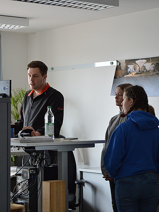 Photo of several young girls at Girls Day in Aichach. They are standing around a colleague's office workstation.