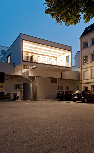 Night shot of a building with external spiral staircase. Wooden extension.