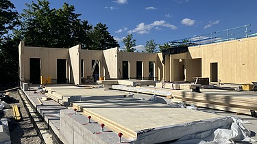 Baustellenfoto, auf dem die Montage der ersten Brettsperrholzelemente zu sehen ist.