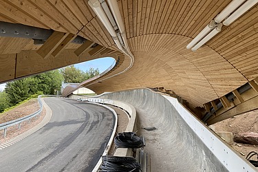 Foto einer Rennrodelbahn. Man sieht eine Holzdachkonstruktion.