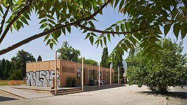 Photo of a wooden building with a flat roof. You can also see graffiti on the wooden façade.