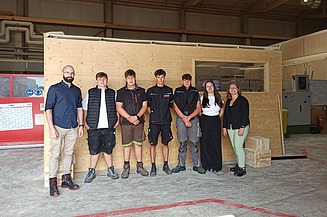 News ZÜBLIN Timber Photo of seven young people starting their apprenticeship or dual study program at ZÜBLIN Timber. They are standing in front of a wooden element in the production hall.