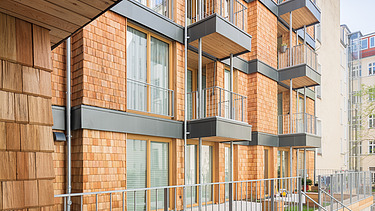Photo of a multi-storey residential complex made of wood. You can see a detailed section of the façade made of wooden shingles.