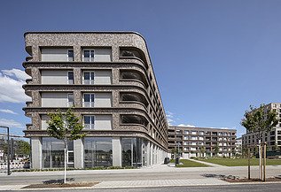 BUGA-Areal Spinelli, Mannheim. Zu sehen ist hier der Holz-Hybrid-Bau B9.1 Foto eines großen mehrgeschossigen Gebäudes mit Holzfassade. BUGA-Areal Mannheim.
