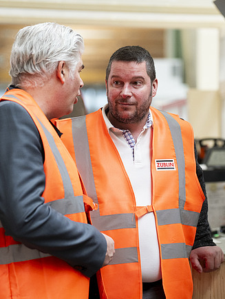Zwei Männer, die sich in der Fertigungshalle von ZÜBLIN Timber unterhalten.