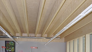 Foto einer Bibliothek von innen. Das Augenmerk liegt hauptsächlich auf der Rippendecke aus Holz.