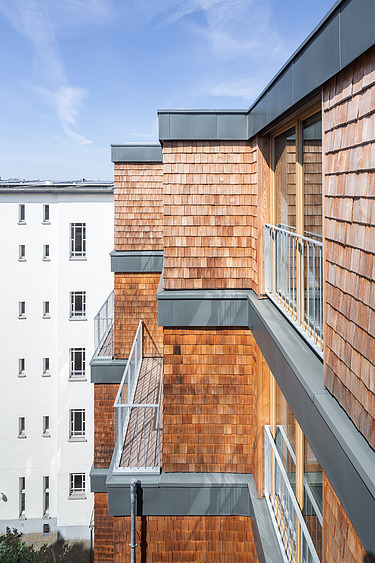 Foto einer mehrgeschossigen Wohnanlage aus Holz. Man sieht einen Detailausschnitt der Fassade aus Holzschindeln.