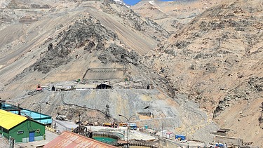 Photo of a barren mountain landscape made of sand. Small houses can be seen in the copper landscape. As well as a blue sky.