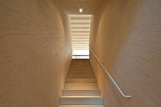 Photo of a wooden staircase with wooden walls in fineline look. Looking upwards.
